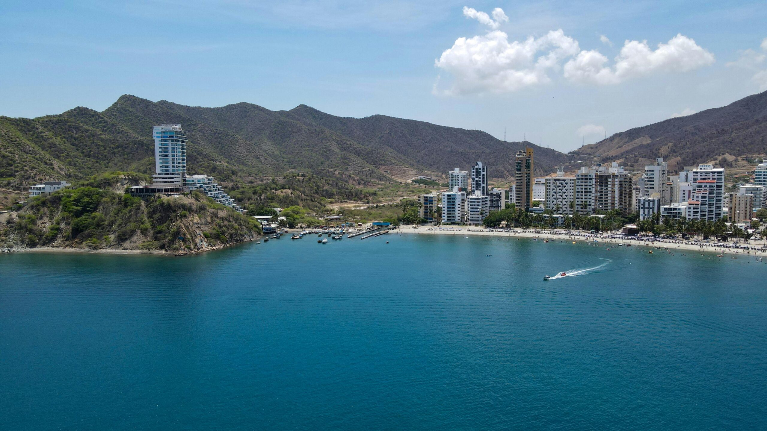 A vibrant coastal city with mountains, beach, and clear blue sea under a sunny sky.